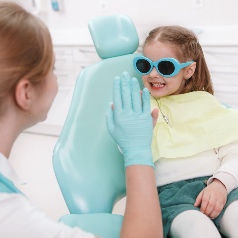 Little girl smiling with glasses on high fiving dentist